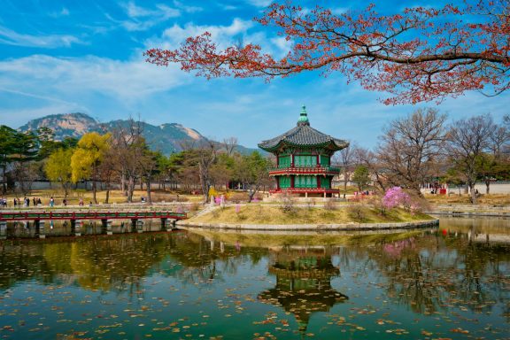 Corea Pabellón tradicional rodeado de lago y árboles en un parque con montañas al fondo.