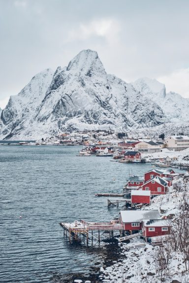 Tromso Paisaje invernal con montañas nevadas y cabañas rojas junto a un fiordo.